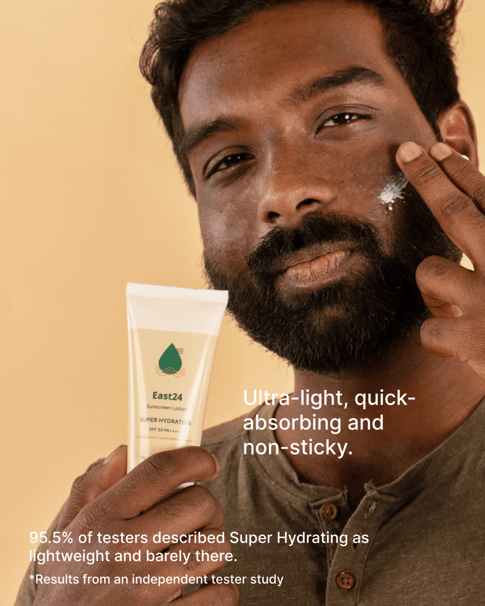 Man applying East24 Super Hydrating SPF 50 PA++++ moisturizing sunscreen to his face with a tube of cream in front of him on a beige background