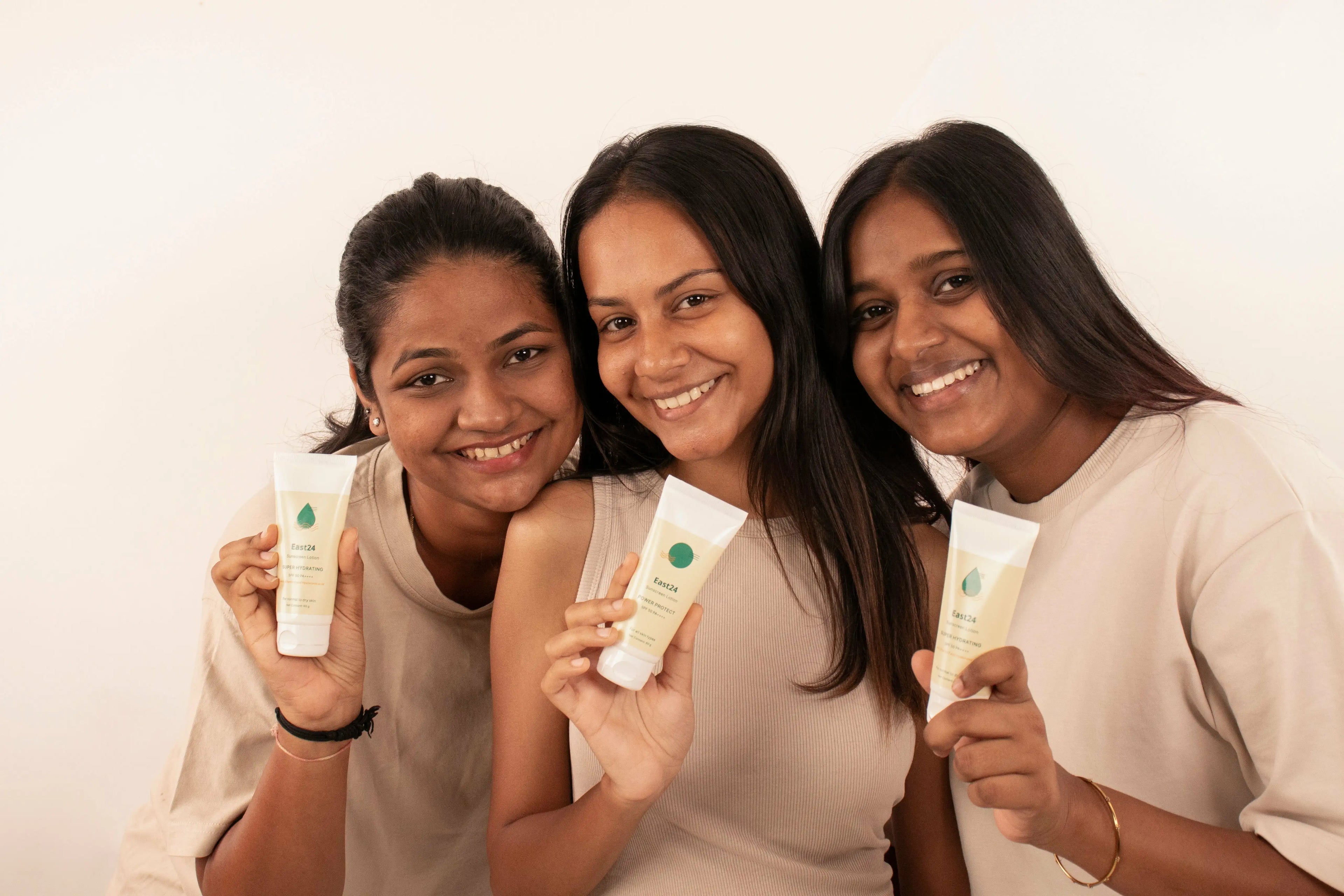 Three women holding skincare products against a white background