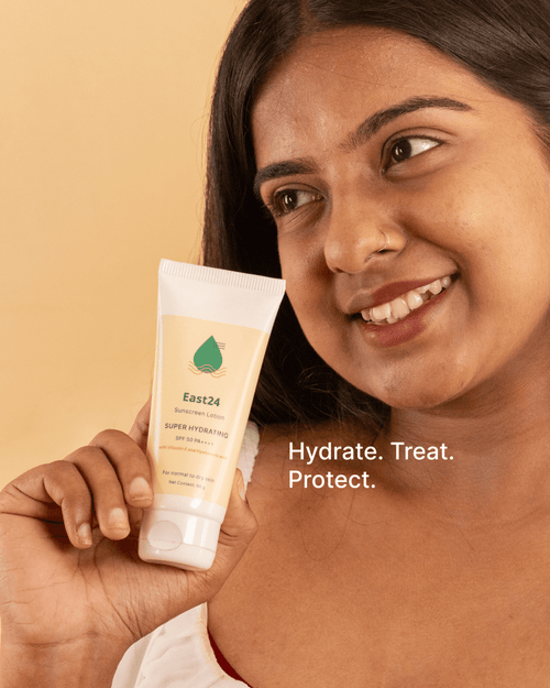 Woman holding a tube of East24 SPF 50 PA++++ moisturizing sunscreen with a beige background